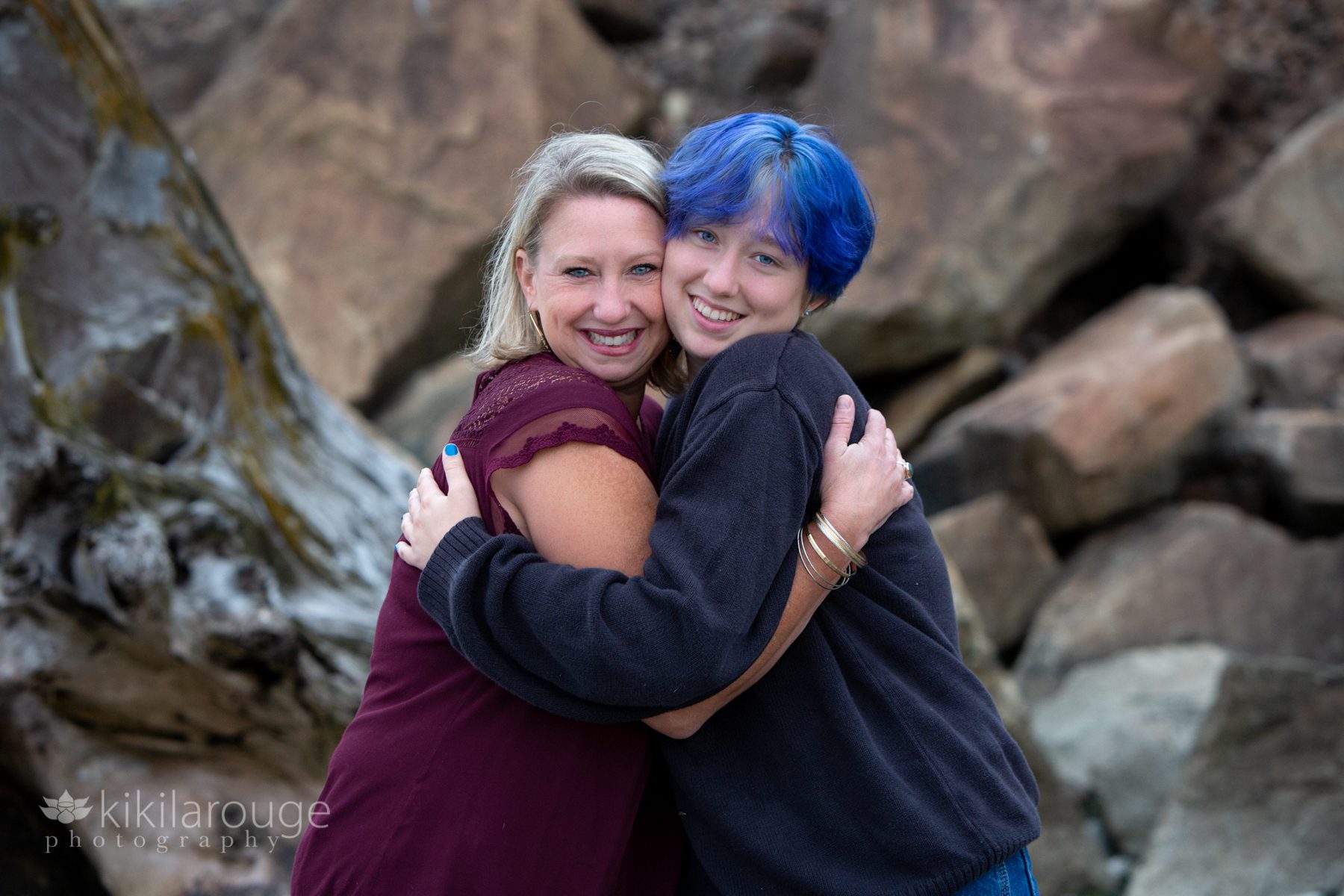 Mom and teen with blue hair hugging at beach
