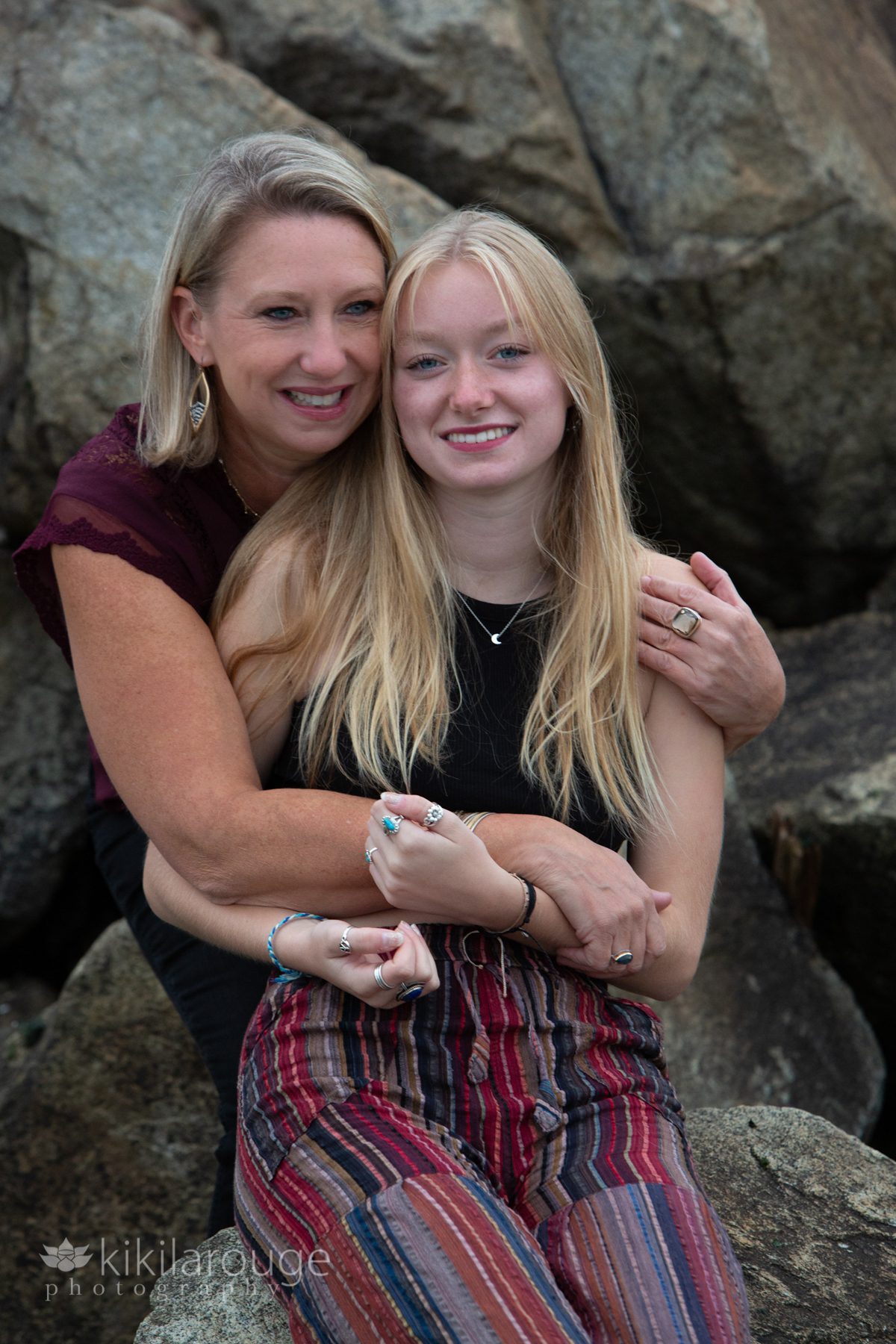 Blonde mother and daughter hugging on rocky beach