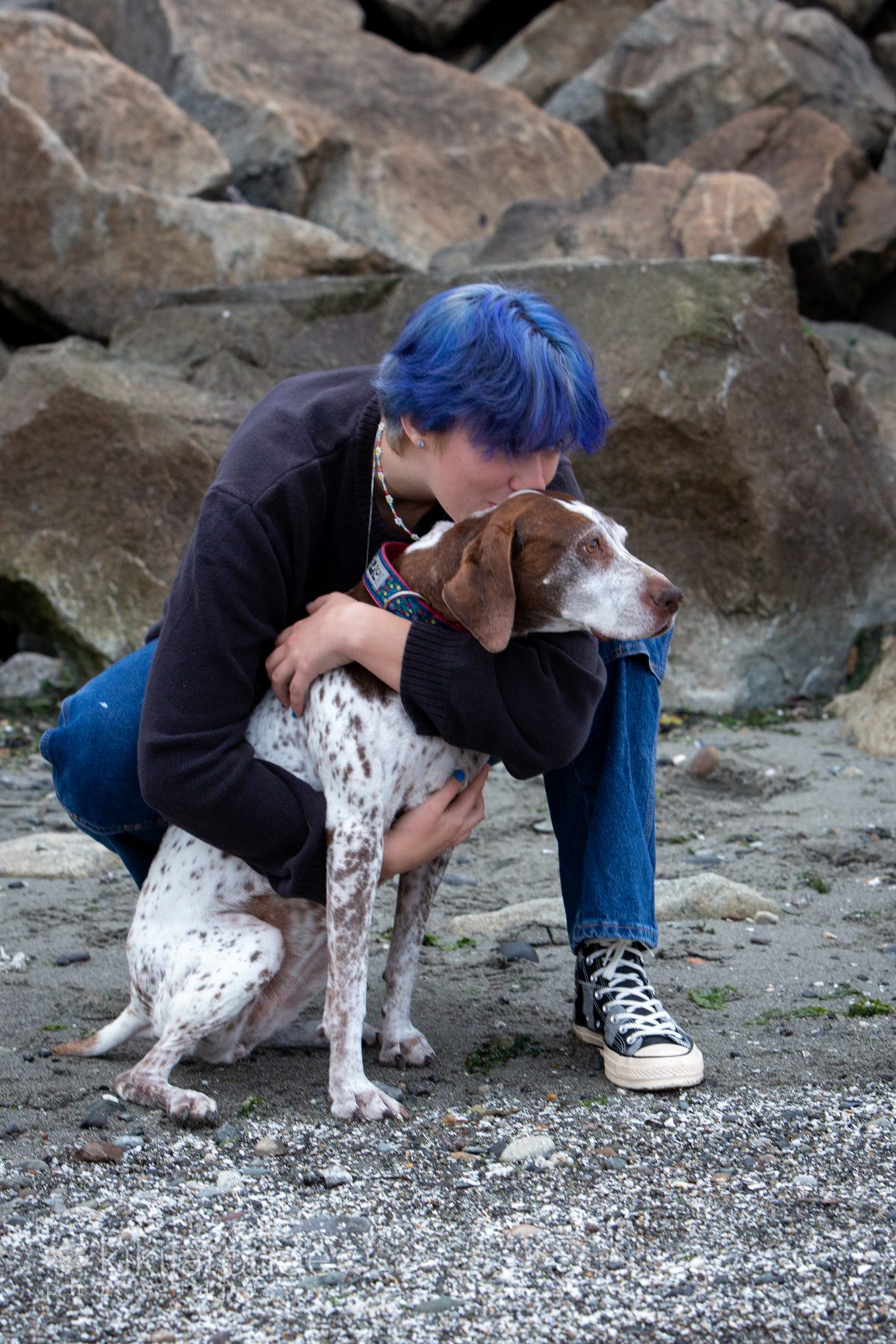 Teen in denims with blue hair hugging GSP dog at beach