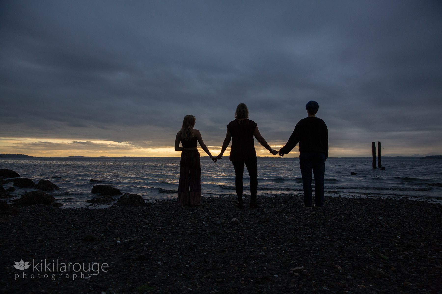 Mom with two teens in silhouette at stormy sunset beach