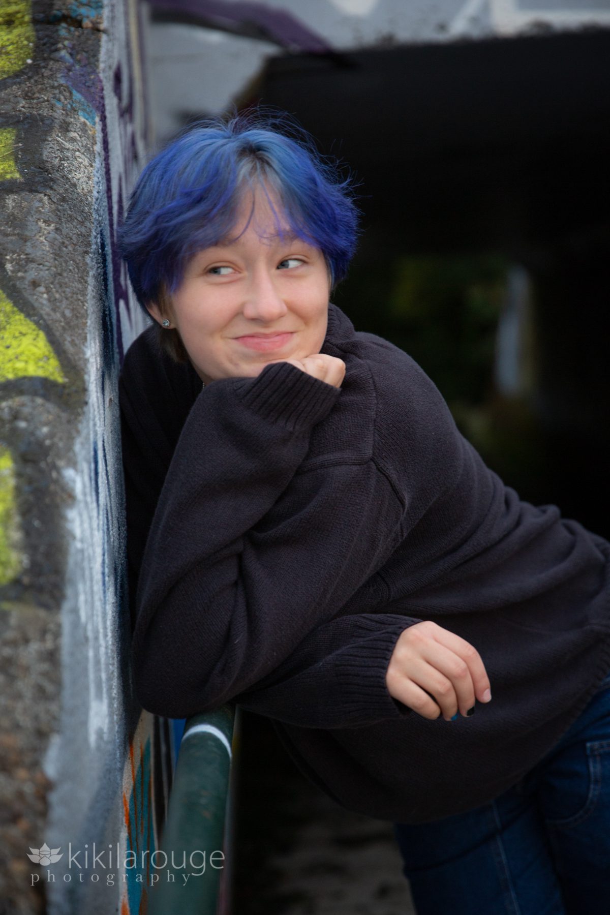 Teen with bright blue hair leaning on railing smiling