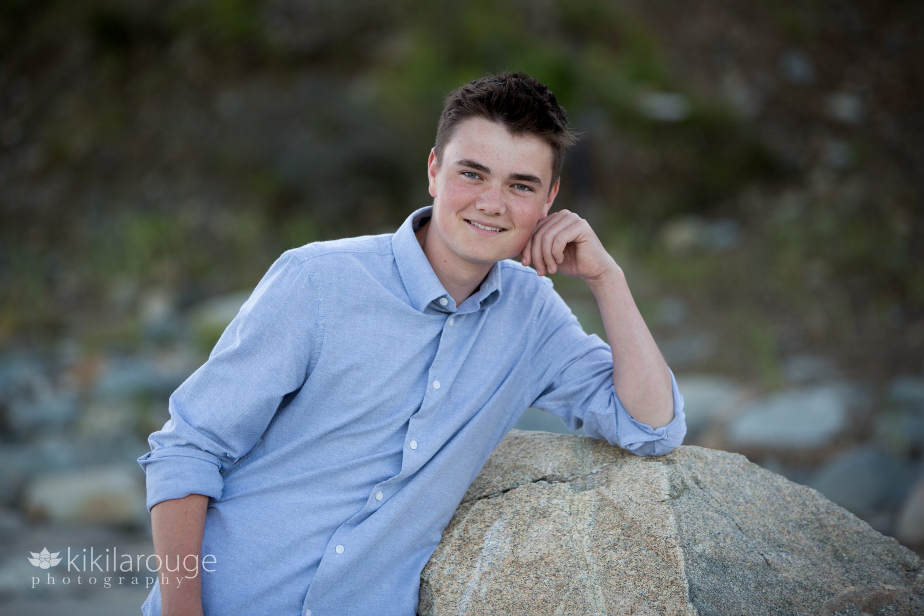 Senior boy leaning and smiling on rock at beach