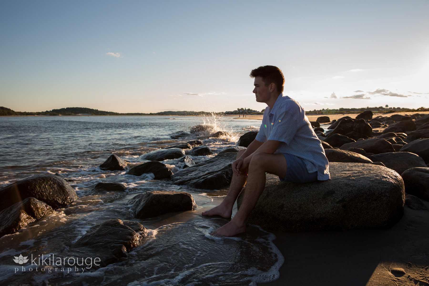 Silhouette of teen boy sitting on rocks at water's edge