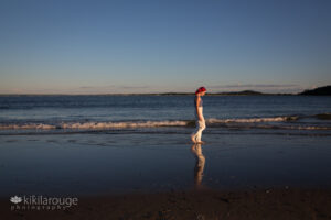 Girl with white pants and bright pink hair walking down beach