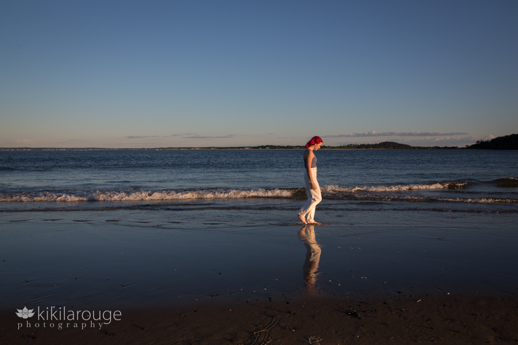 Girl with white pants and bright pink hair walking down beach