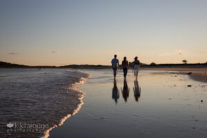 Family of three in silhouette walking towards sunset at beach