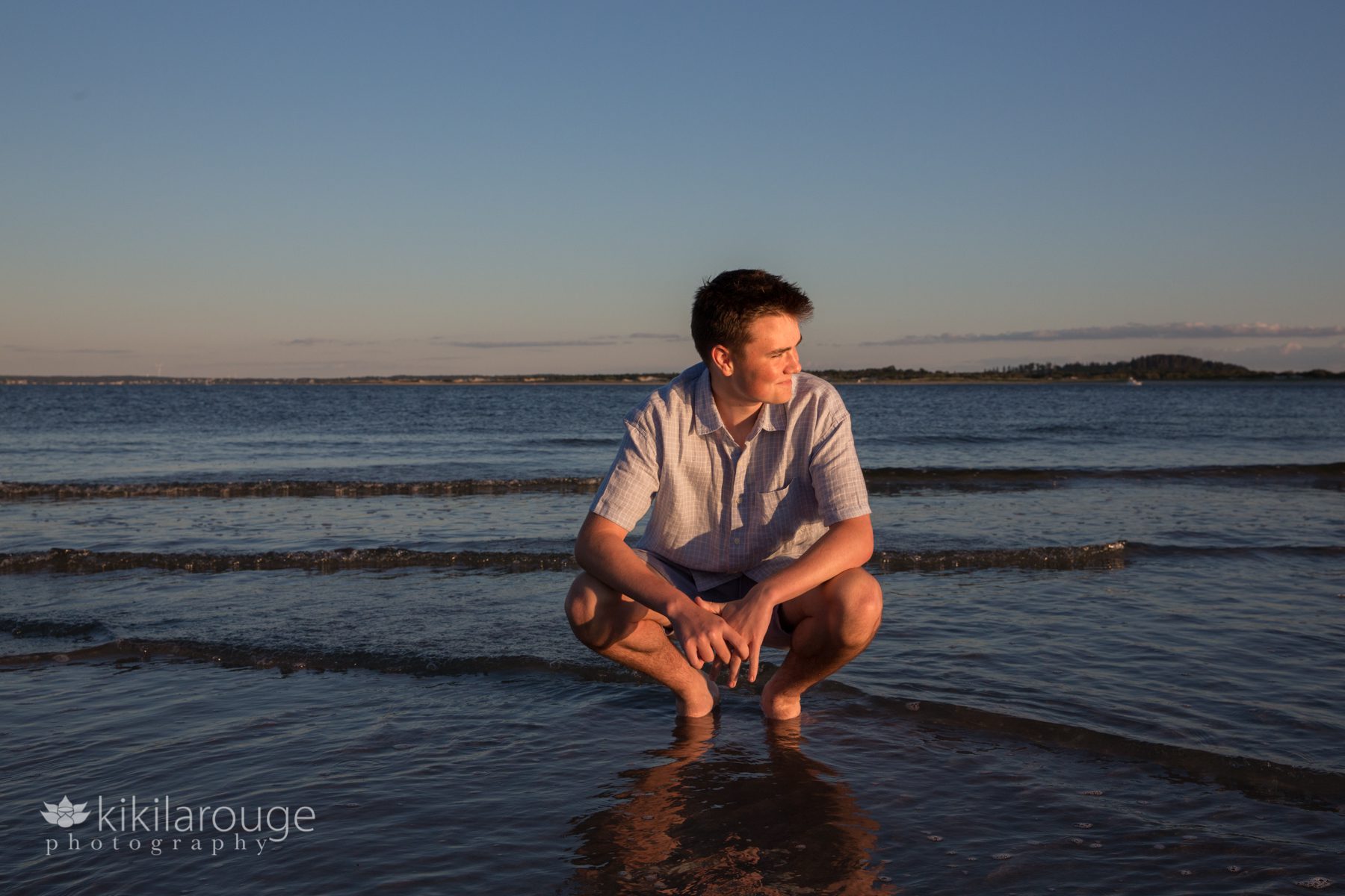 Boy in water at beach crouched down looking to the left