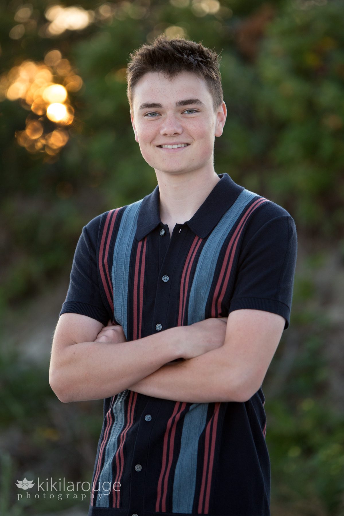 Senior boy in striped short sleeved sweater with sunsetting behind beach dunes