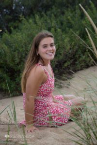 Pretty teen brunette girl in floral red dress hair blowing sitting in dune