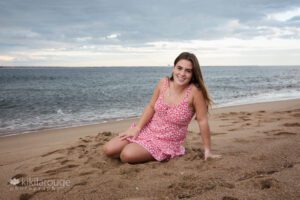 Teen girl long brunette hair in floral red dress sitting on beach