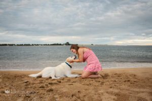 Teen girl in floral dress at beach looking at yellow lab dog