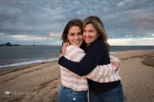 Teen girl and mom hugging at beach with dramatic skyline