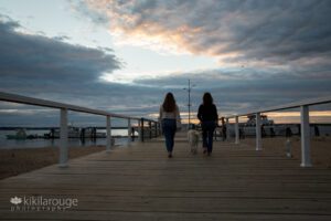 Girl and her Mom and dog walking into sunset on pier