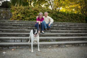 Couple sitting on stone steps in jeans holding leash with black and white rescue dog in front