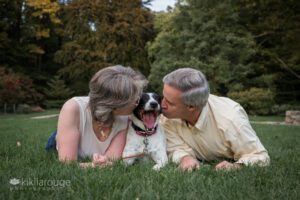 Couple laying on lawn with yawning dog in the middle
