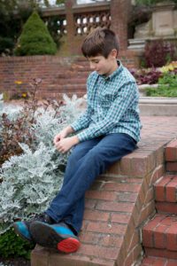 Young boy in plaid shirt sitting on brick stairway looking at plant