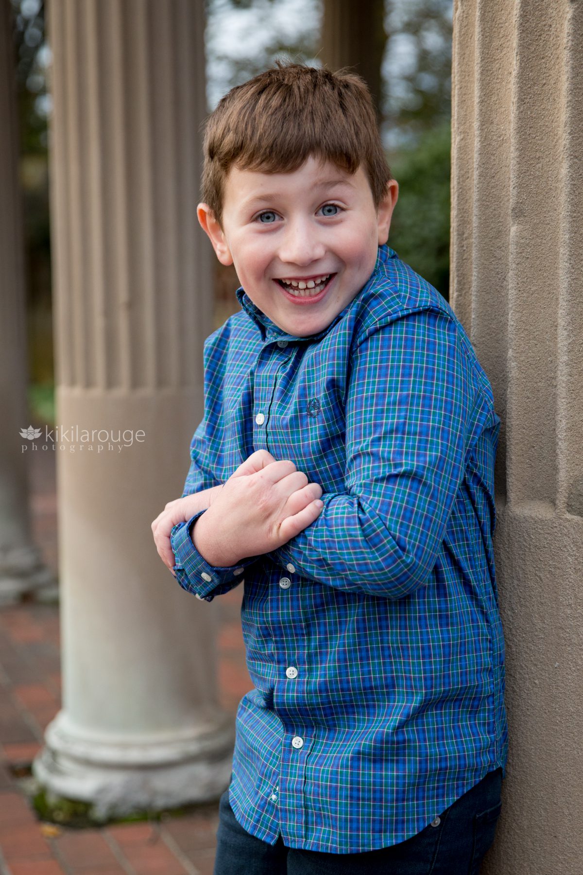 Little boy in blue shirt smiling leaning on column in rose garden