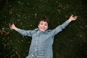 Boy laying in the grass with fall leaves