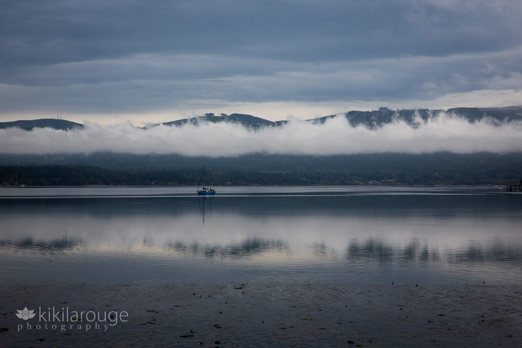 Lone boat in water with clouds over mountains and reflected in bay