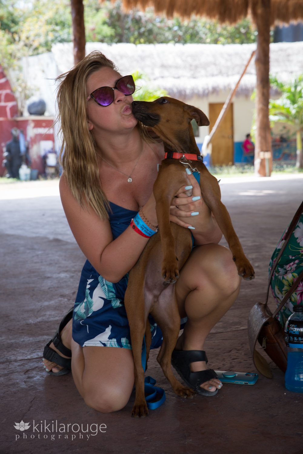 Girl with sunglass and tropical dress kissing a brown rescue pup in gazebo