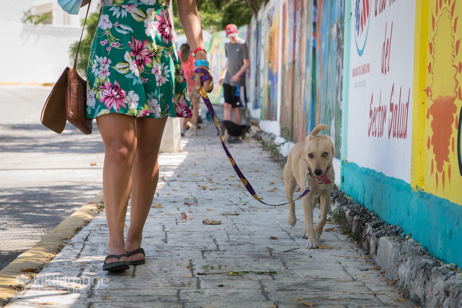 Girl in green floral sundress walking tan puppy on Mexican sidewalk