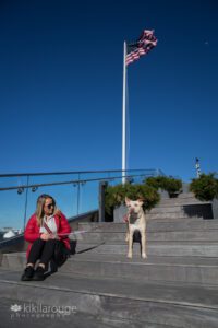 Foster mom with Mixed breed yellow lab dog sitting on harbor steps in Boston with American flag waving