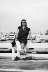 Mom sitting on pier with young son sitting below hugging her leg