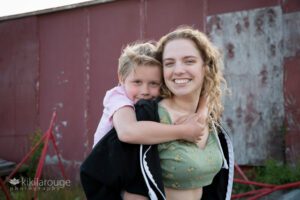 Young boy on back smiling with his aunt in half green top and sweatshirt