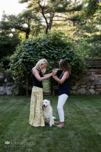 Cute couple blonde and brunette women with their white lab dog in garden
