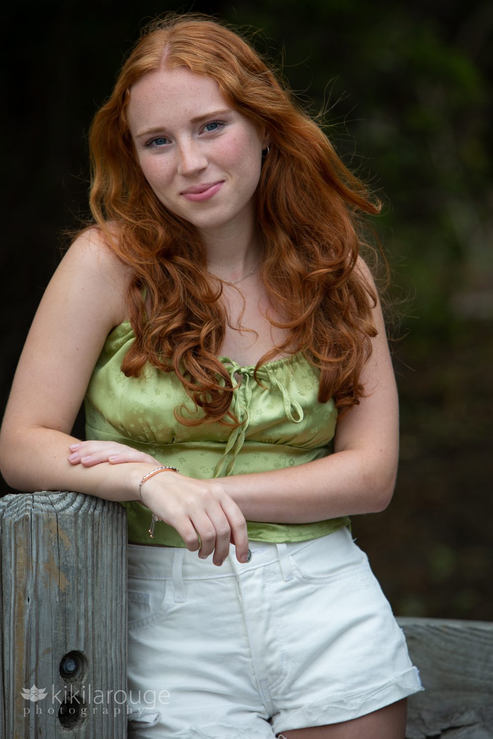 Redheaded teen senior portrait Sandy Point with hair blowing in green tanks top and white shorts