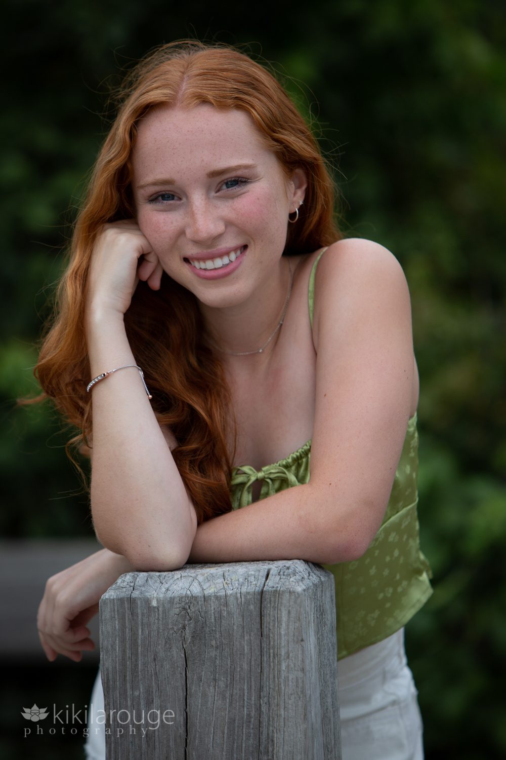 Senior portrait girl with red hair and green silk tank top leaning on wood post