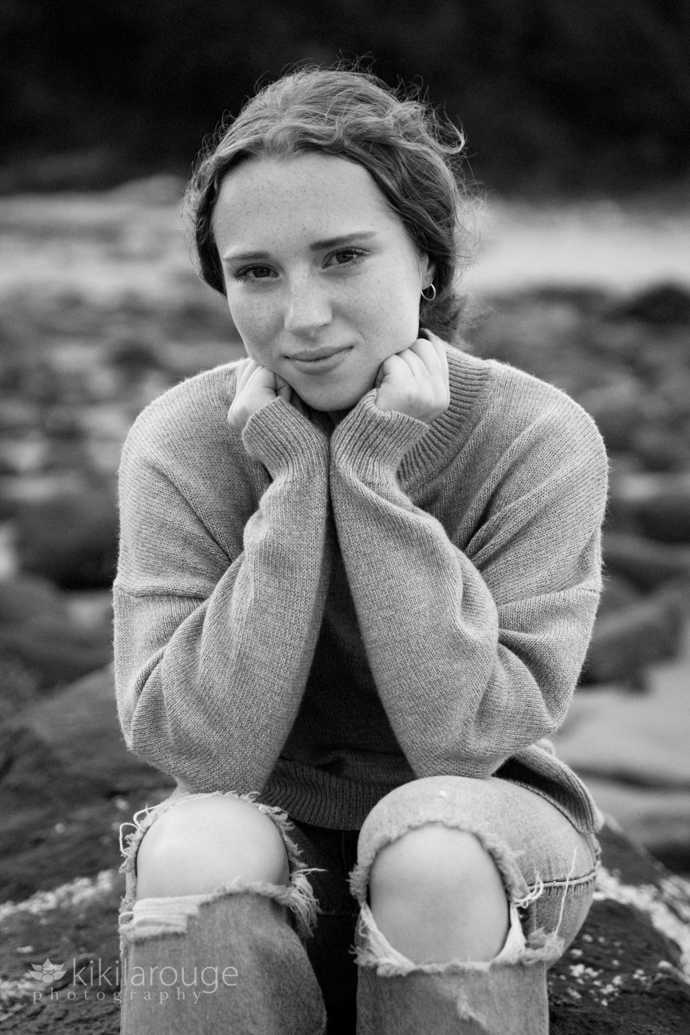Girl sitting on beach rock with hands under chin hair pulled back