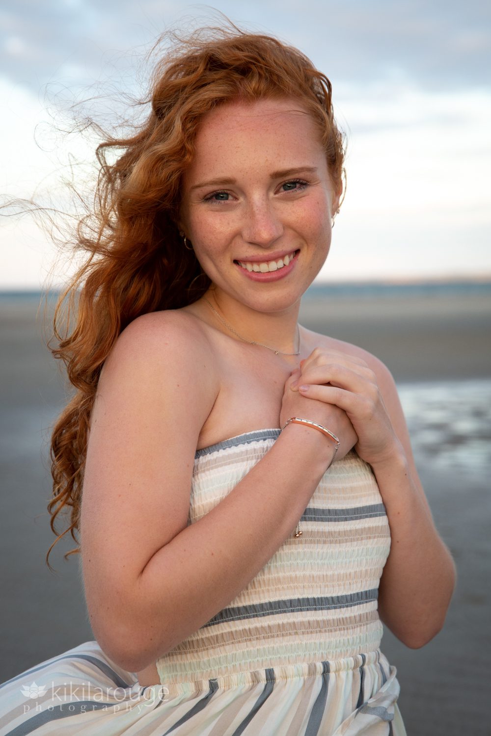 Portrait of a redhead with hands in heart on chest smiling at sunset