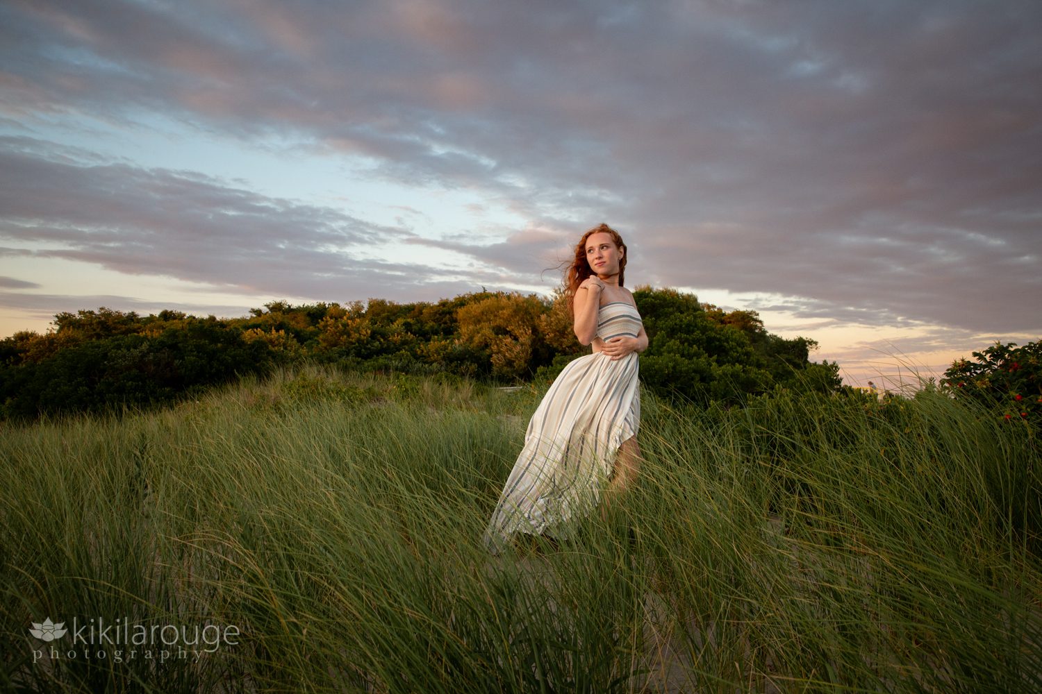 Landscape of dramatic sunset with redheaded girl in flowing dress in dunes