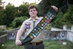 Teen boy holding Eagle Scout sash with badges close to camera