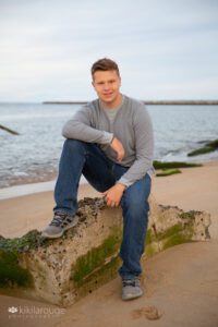 Senior boy sitting on cement barrier at Plum Island beach