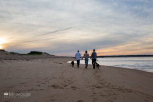 Family walking into the sunset at Plum Island beach with two black dogs