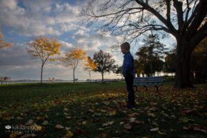 Silhouette of young boy standing on grass looking out on the ocean fall foliage