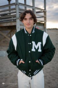 Senior portrait teen boy curly brown hair in green letterman jacket with white M