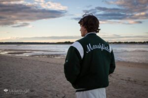 Boy with green high school Marshfield jacket on facing sunset with clouds
