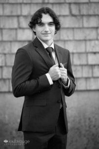 Teen boy BW portrait holding suit jacket by weather wall
