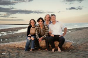 Family of four with Mom Dad and two teens sitting on driftwood at beach during sunset