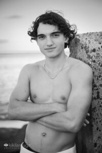 Handsome teen boy with no shirt at beach leaning on cement barrier