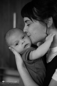 Mom with dark hair holding her two month old baby kissing his cheek