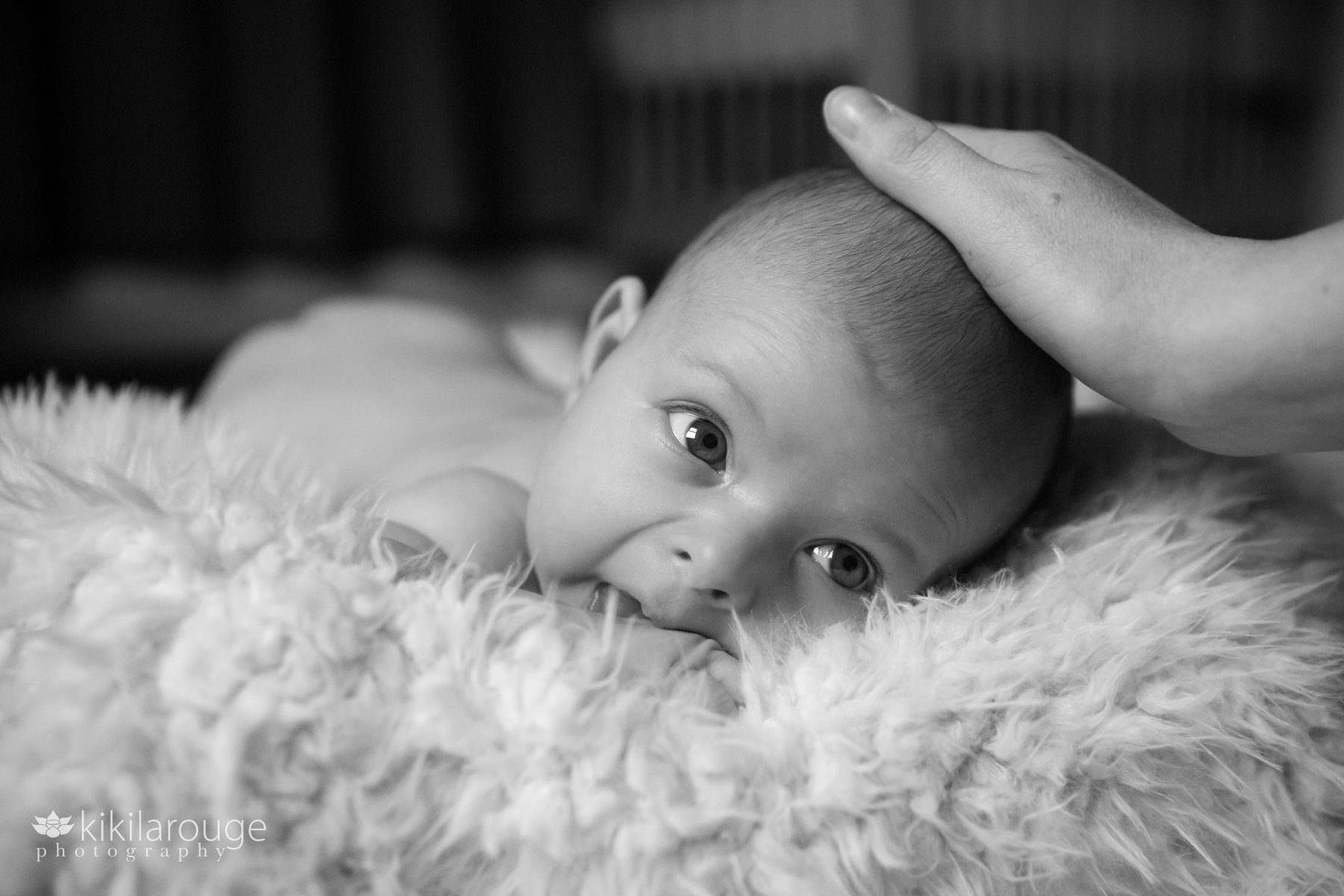 Mom soothing baby who is looking at her while laying on white blanket