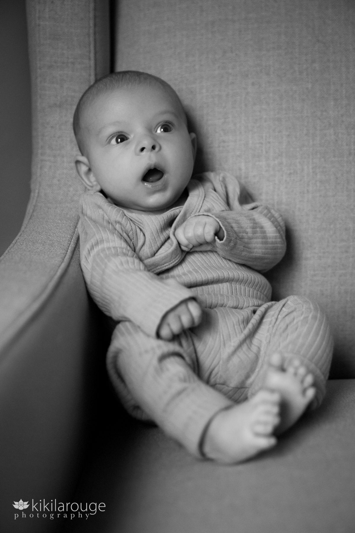 Baby with wow expression sitting upright in gray chair