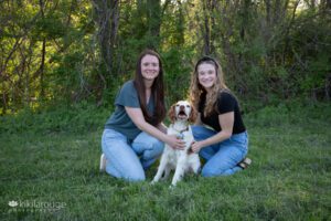 Two young women in jeans with their Brittnay Spaniel dog in the middle
