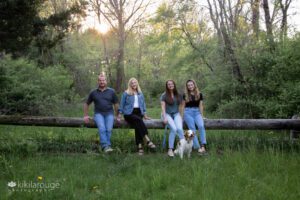 Family Portrait of four people sitting on log in forest with Brittnay Spaniel family dog in front