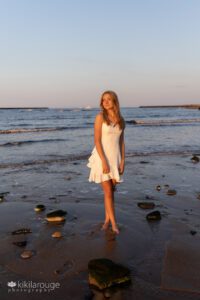 Girl in white dress in water at Plum Island beach looking at sunset