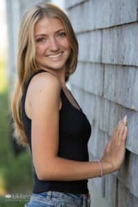 Teenage blonde Senior In jean shorts and black tank top standing by weathered shed
